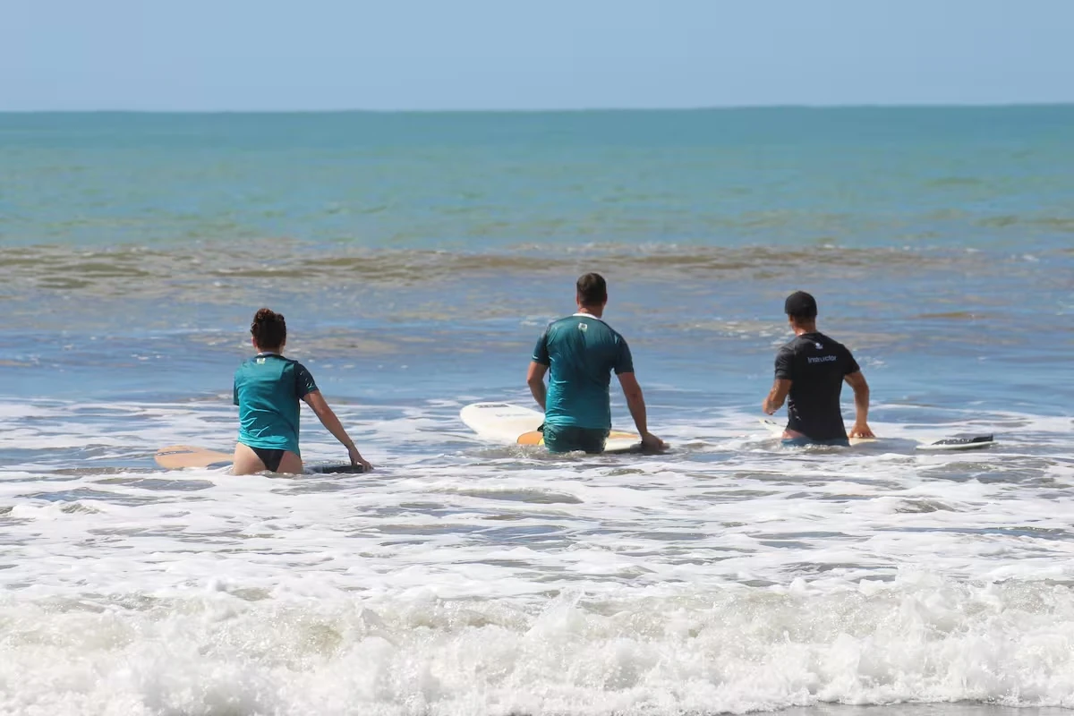 A surf instructor and two surfers sitting on their boards in the whitewater
