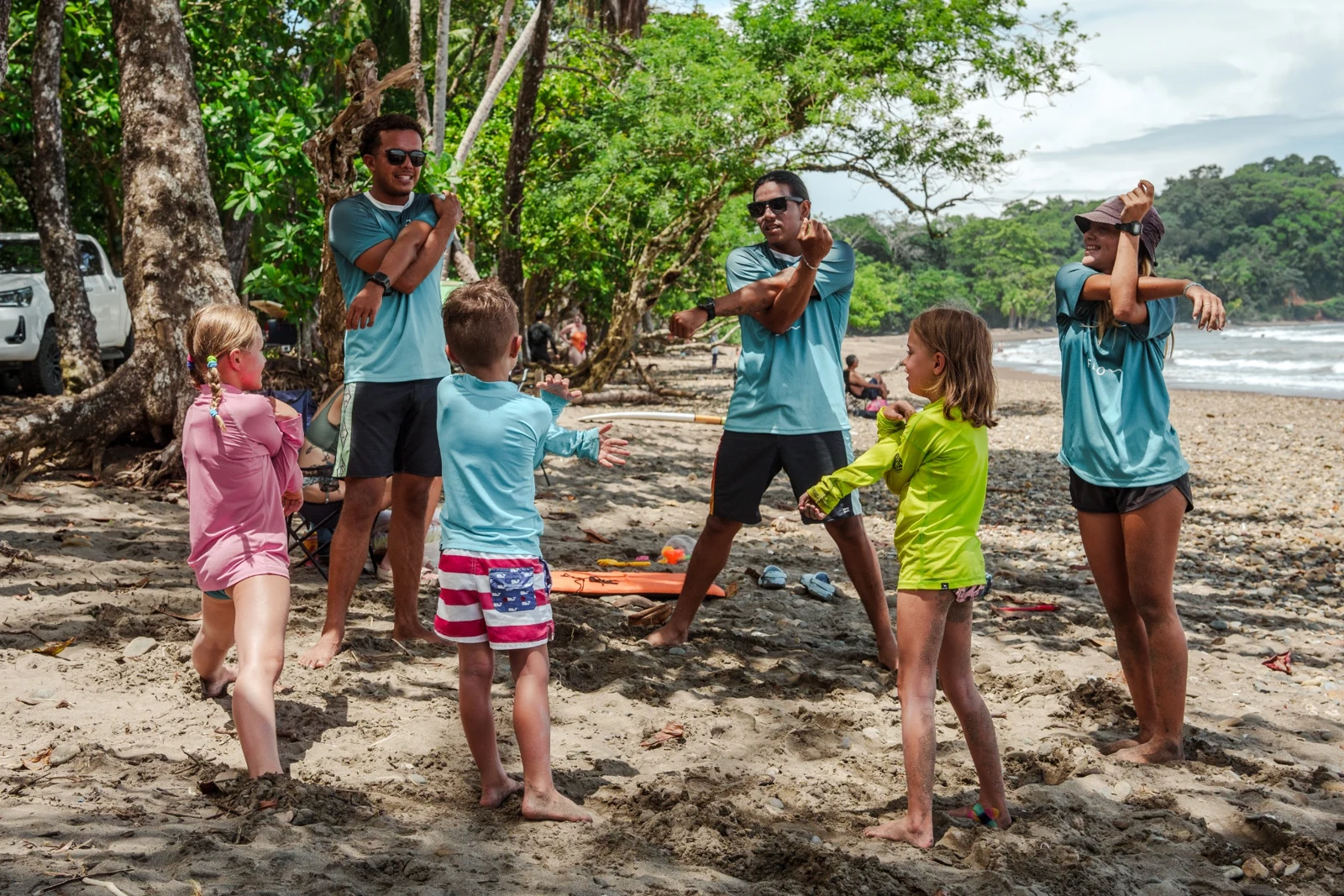 Flow coaches and children warming up together on the beach before a surf lesson