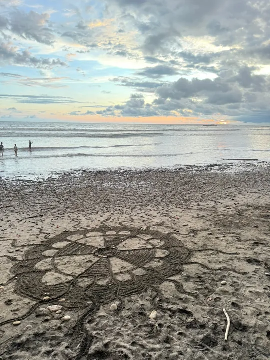 A circular pattern in the beach sand beside calm water