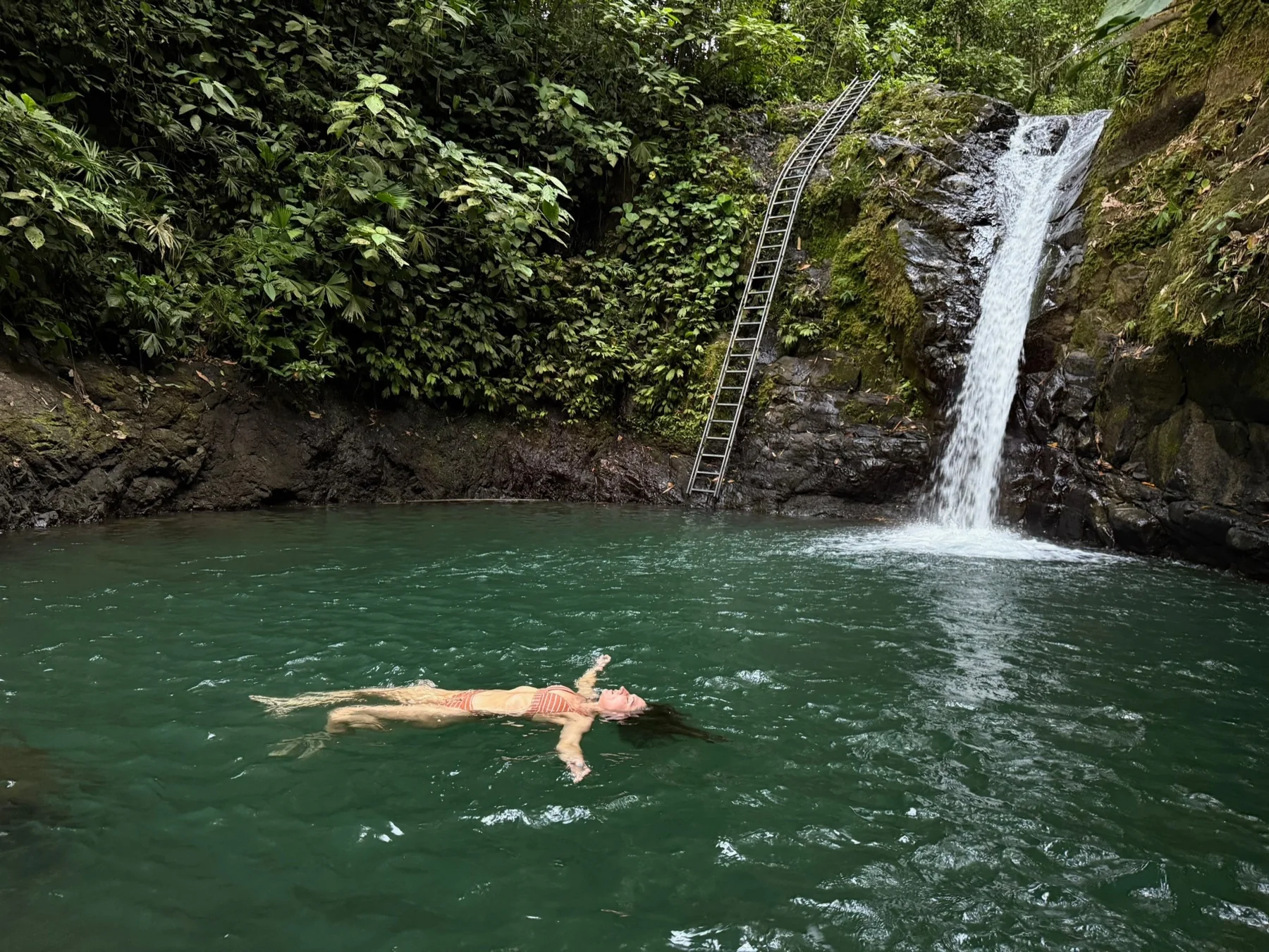 Swimmer floating in a green waterfall pool