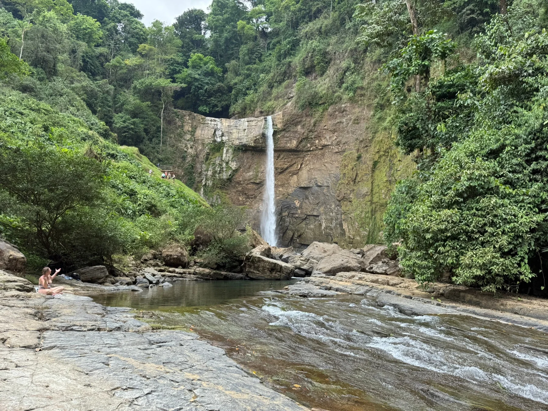 Waterfall surrounded by rainforest, with a rocky river in the foreground