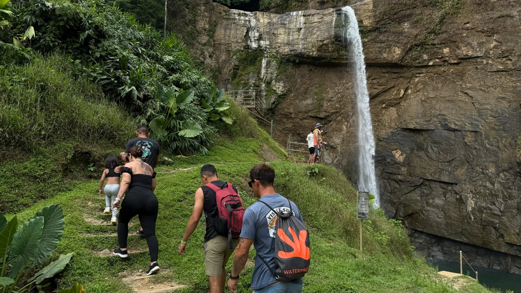 Hikers approaching a waterfall along a green trail