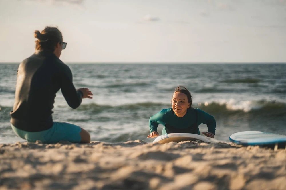 A beach surf lesson with a coach and smiling student