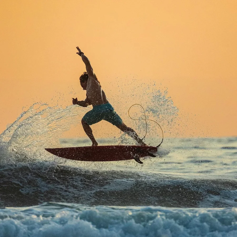 A surfer and red board above a wave at sunset