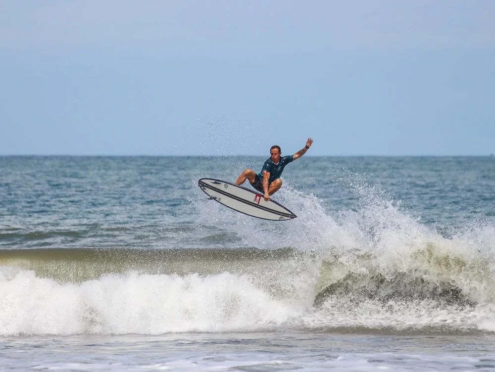 A surfer lifting a white board above the wave